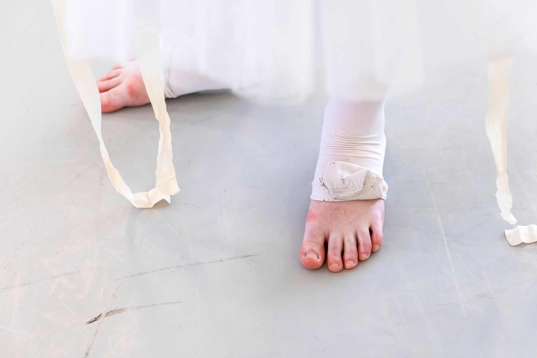 Detailed close-up of a ballerina's bare feet and white tutu ribbons on a dance floor.