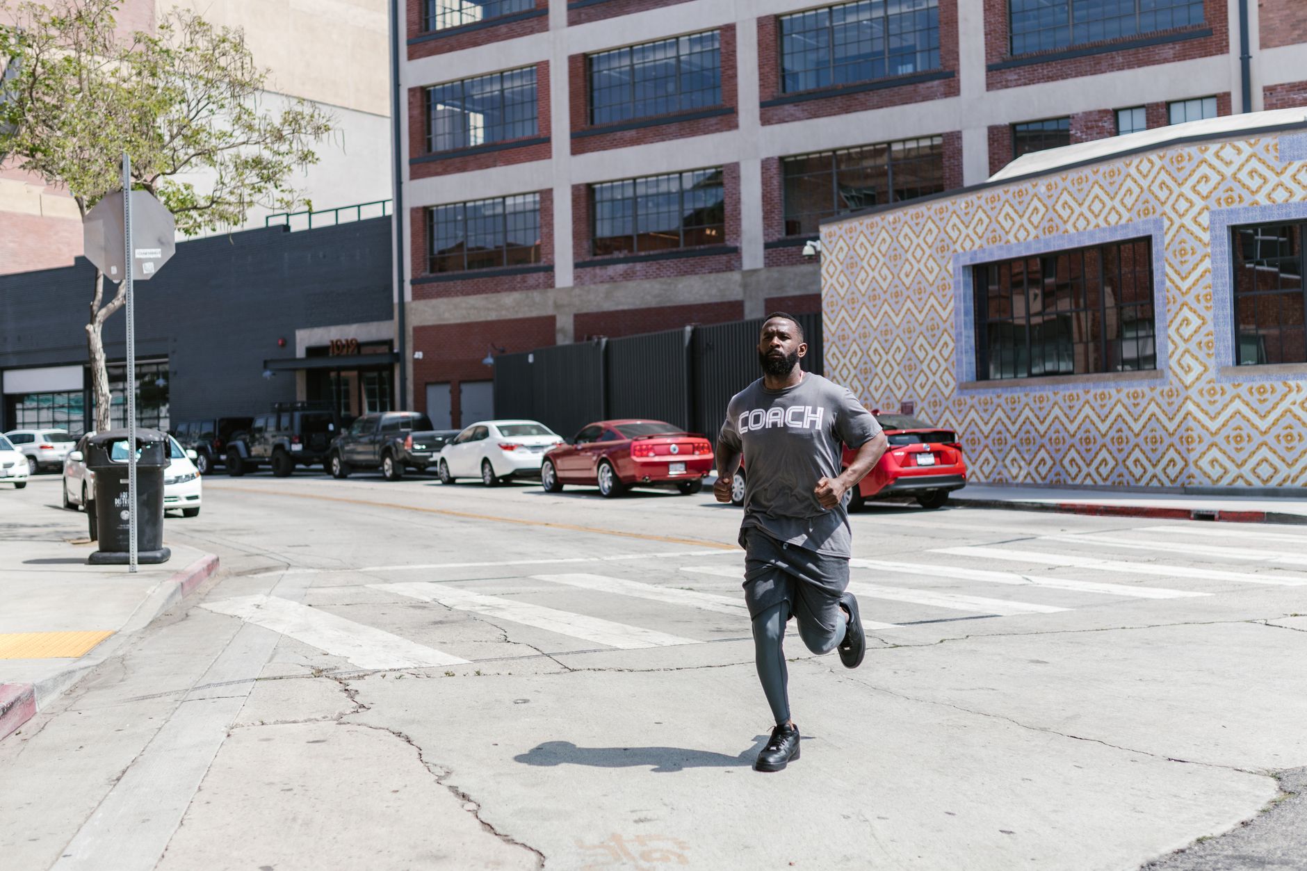 Black man jogging through city streets in sportswear, showcasing fitness and healthy lifestyle.