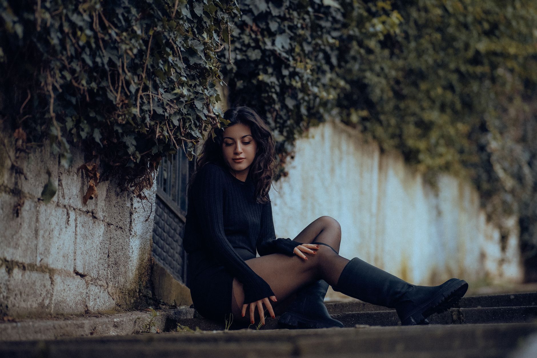Stylish young woman in black outfit sitting on steps in Fethiye. Trendy urban fashion shot.