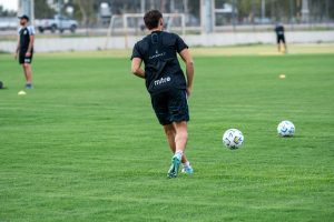 A soccer player practicing dribbling on an outdoor field during the day.