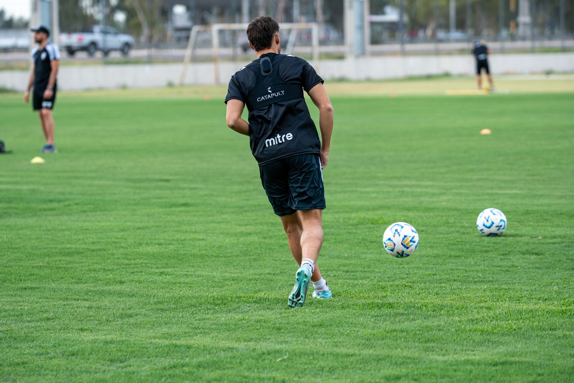 A soccer player practicing dribbling on an outdoor field during the day.