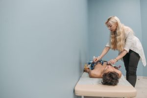 A healthcare professional performs an electrocardiogram on a patient lying on a clinic bed.
